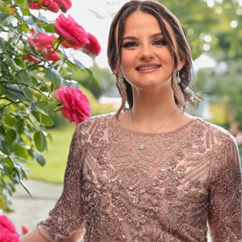 Young woman in beige sequined top smiling near vibrant pink roses in a garden setting
